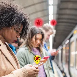 COVID symbols over commuters on subway platform, looking at their phones